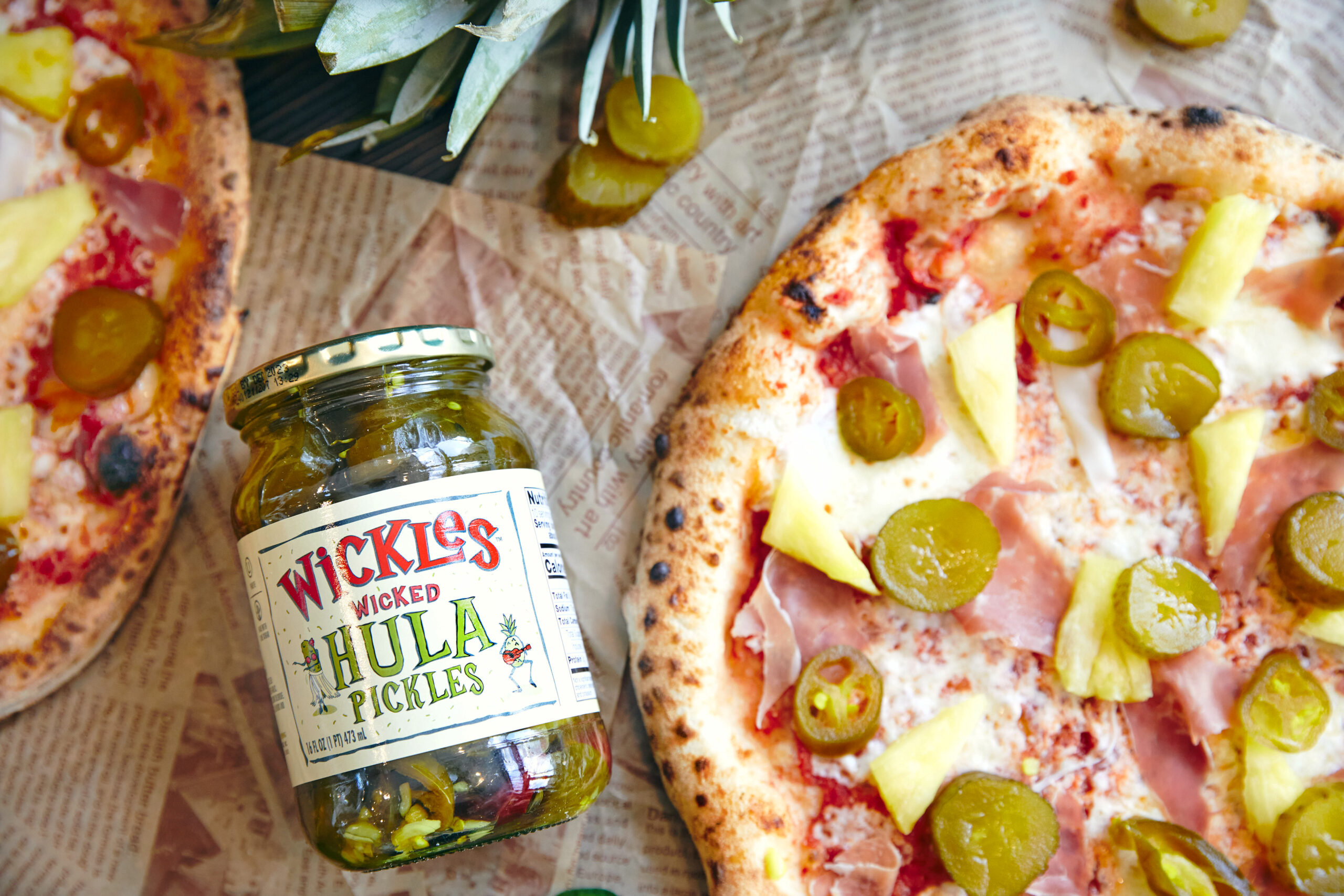 Closeup of a jar of wickles hula pickles next to pizza topped with wickles hula pickles