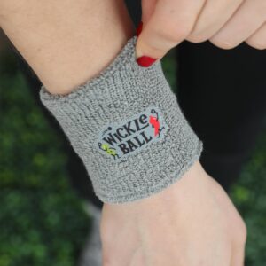 Close up of an arm that has a gray exercise Wristbands with Wickle Ball written on it and a pickle character playing pickleball with a pepper character