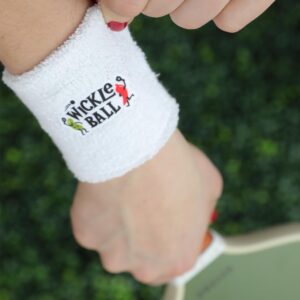 Close up of an arm and hand holding a racket. The arm has a white exercise Wristbands with Wickles, Wickedly Delicious written on it and a Wickles Pickle pickle character dancing with a Wickles Pepper character
